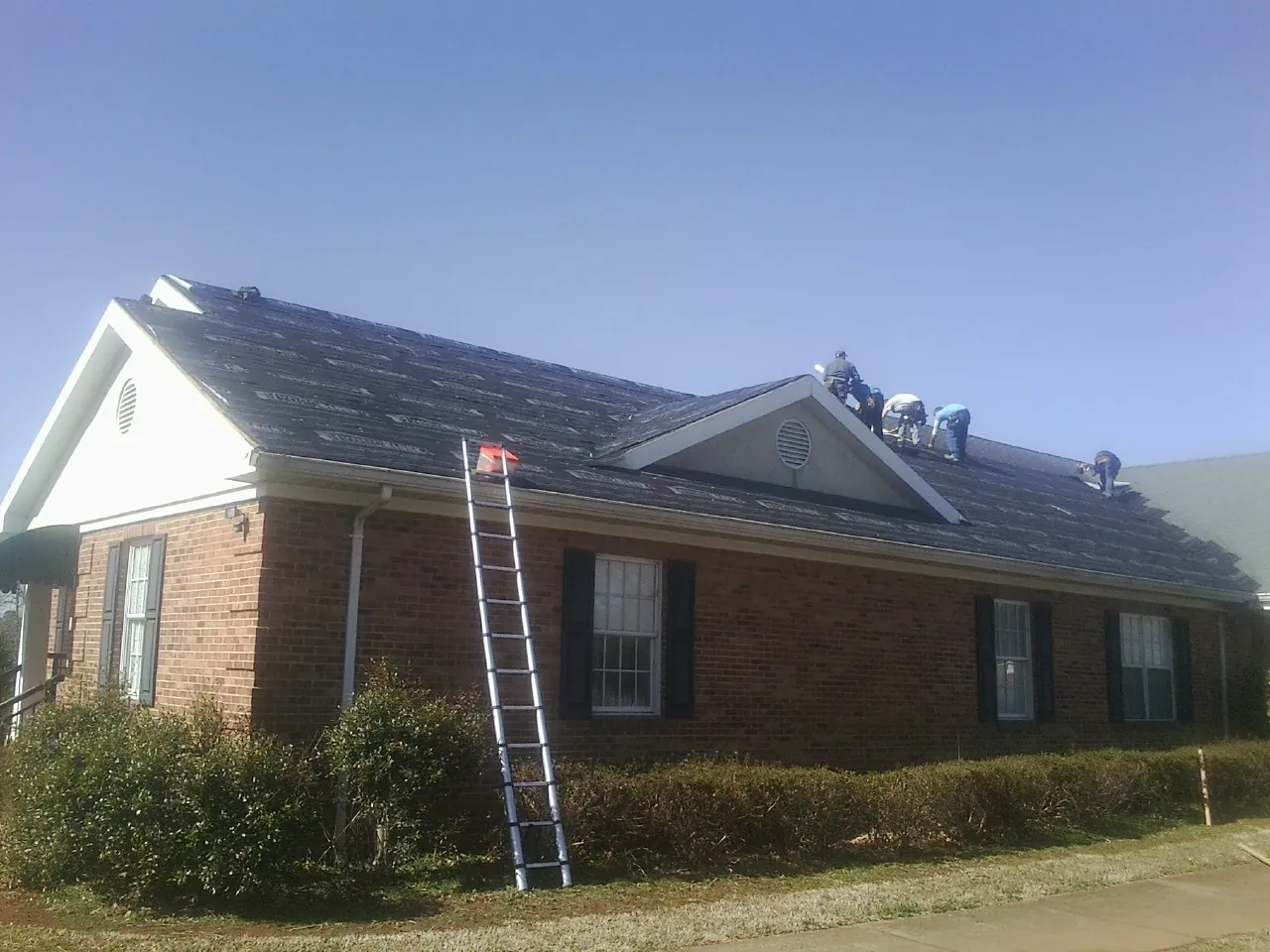 Crew tearing shingles off a brick ranch roof with a ladder set — Metal Roof Repair work by our crew in Pablo