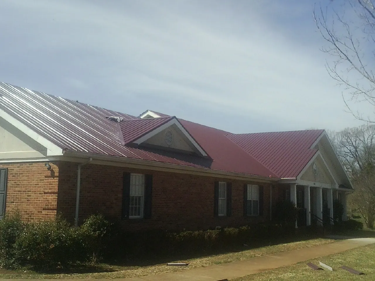 Red metal roof with gabled entries on a long brick building, from a Hail Damage Roof Repair job in Pablo