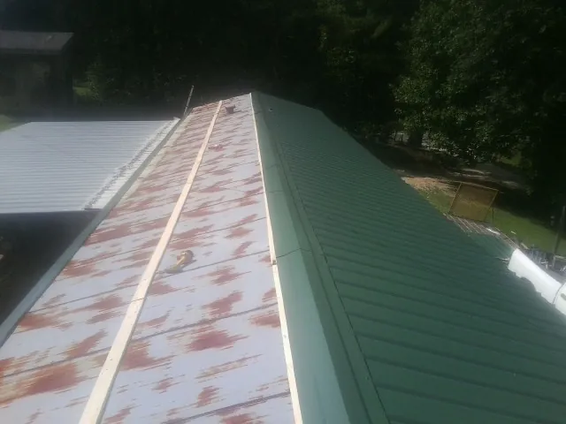 Old rusted panels beside newly installed green metal roofing — Wind Damage Roof Repair by Roofing Brothers in Pablo