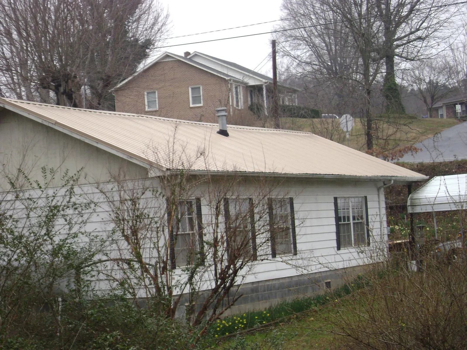 Tan metal roof on a white sided house set into a hillside — Commercial Roofing by Roofing Brothers in Pablo